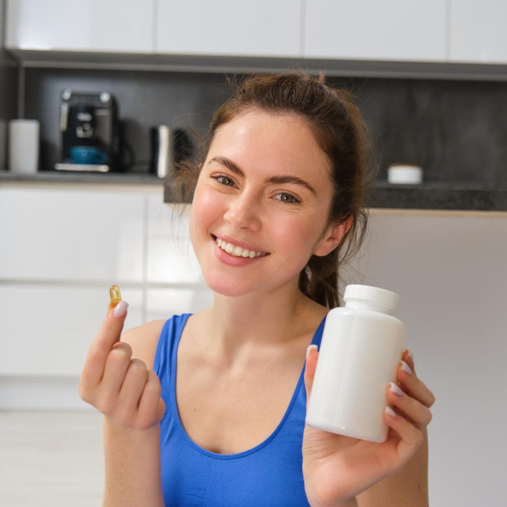 Woman holding a supplement pill and bottle in a kitchen setting